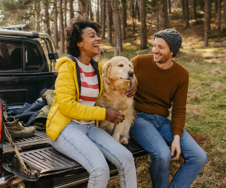 two people with their dog sitting on the tailgate of their truck