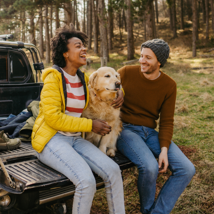two people with their dog sitting on the tailgate of their truck