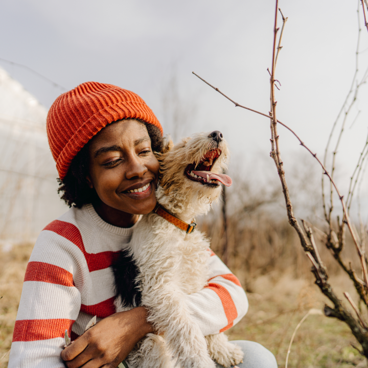woman in an orange beanie hugging her dog